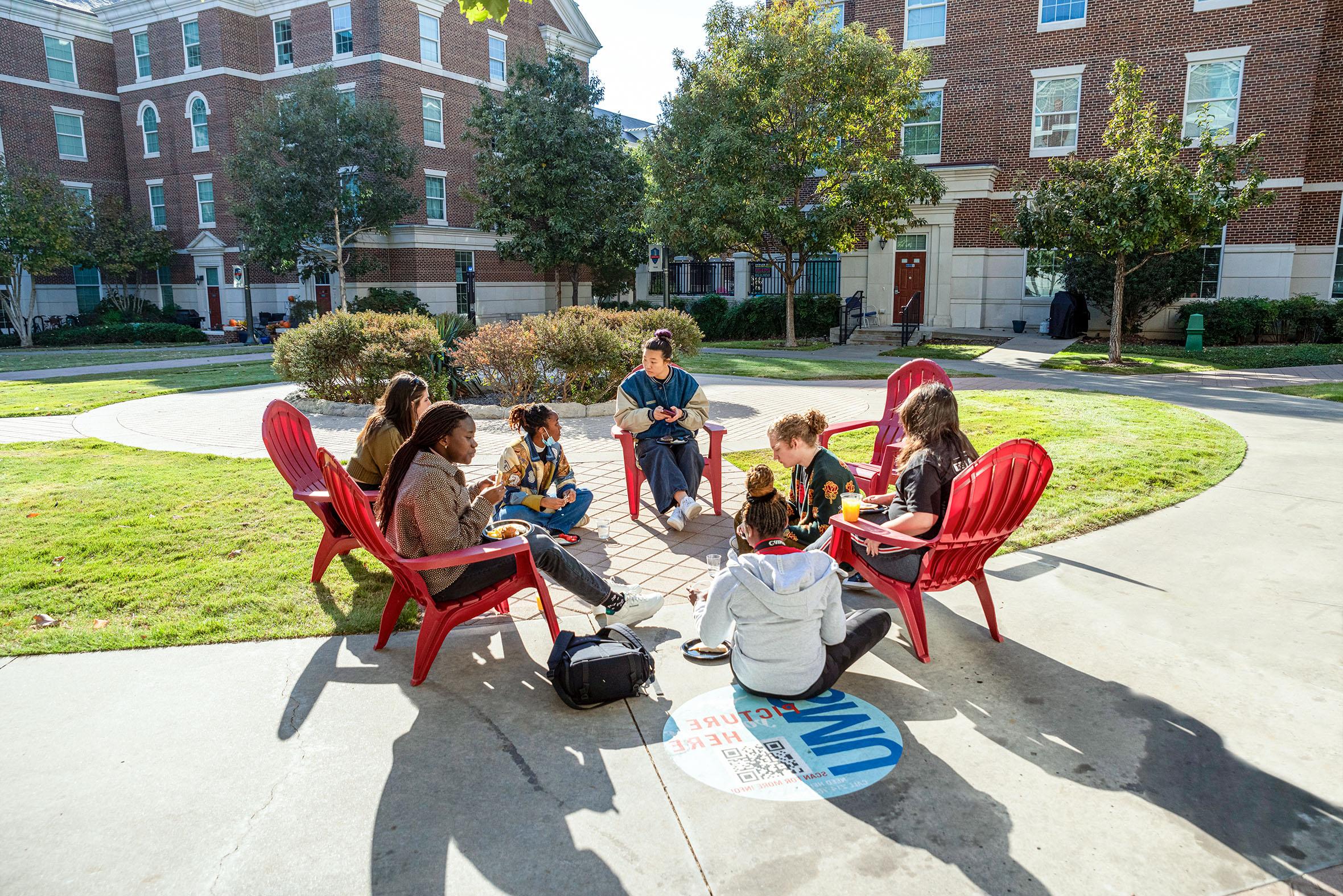 seven students sitting outside in red chairs